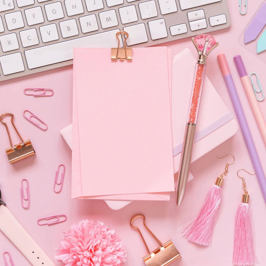 Flat lay of a pink desk with a blank notepad, rose gold clips and a crystal pen, ready for planning nail product label designs